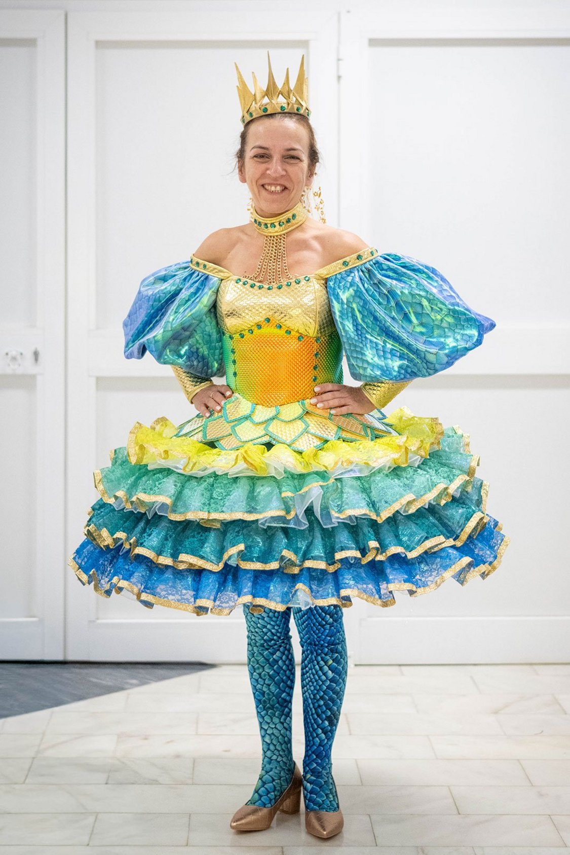 Figurino de Ofiúsa, vestido em tons de dourado e azul, saia com tule cheio de texturas, coroa dourada na cabeça, collants padrão serpente